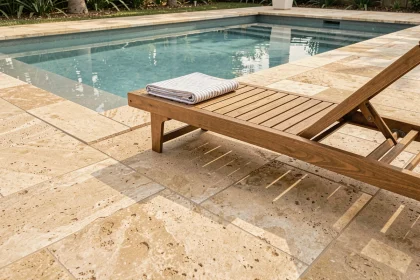 Abords de piscine aménagés avec des dalles antidérapantes en grès beige et un transat en bois teck